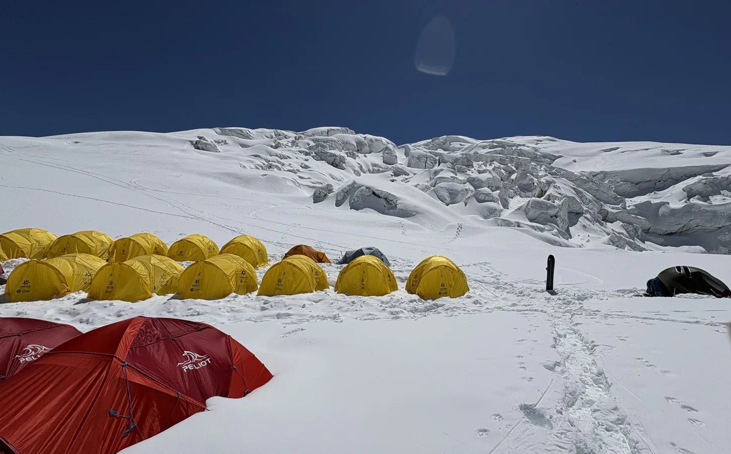 Rows of expedition tents below broken glacier seracs under a deep blue sky.