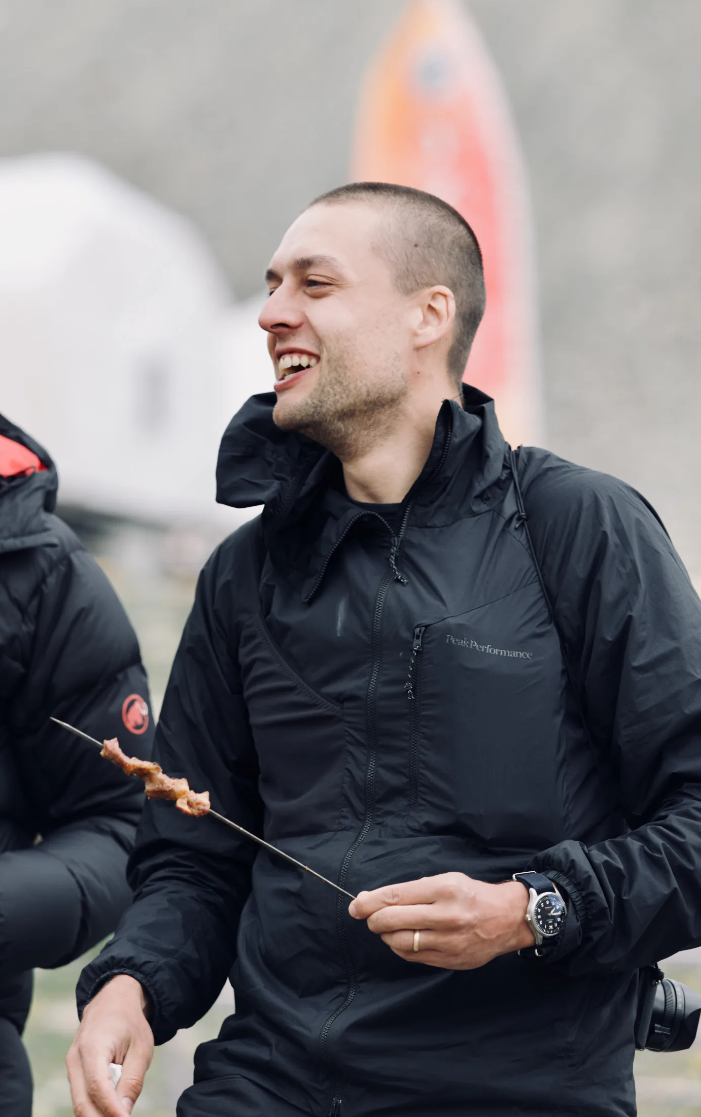 A smiling expedition member holding a barbecue skewer during a relaxed moment at camp.