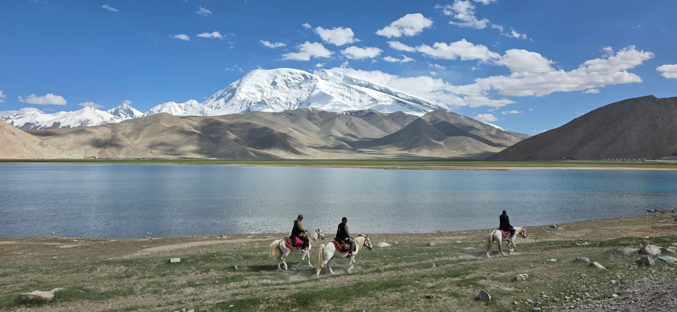 Travellers moving along the shore beneath Muztagh Ata