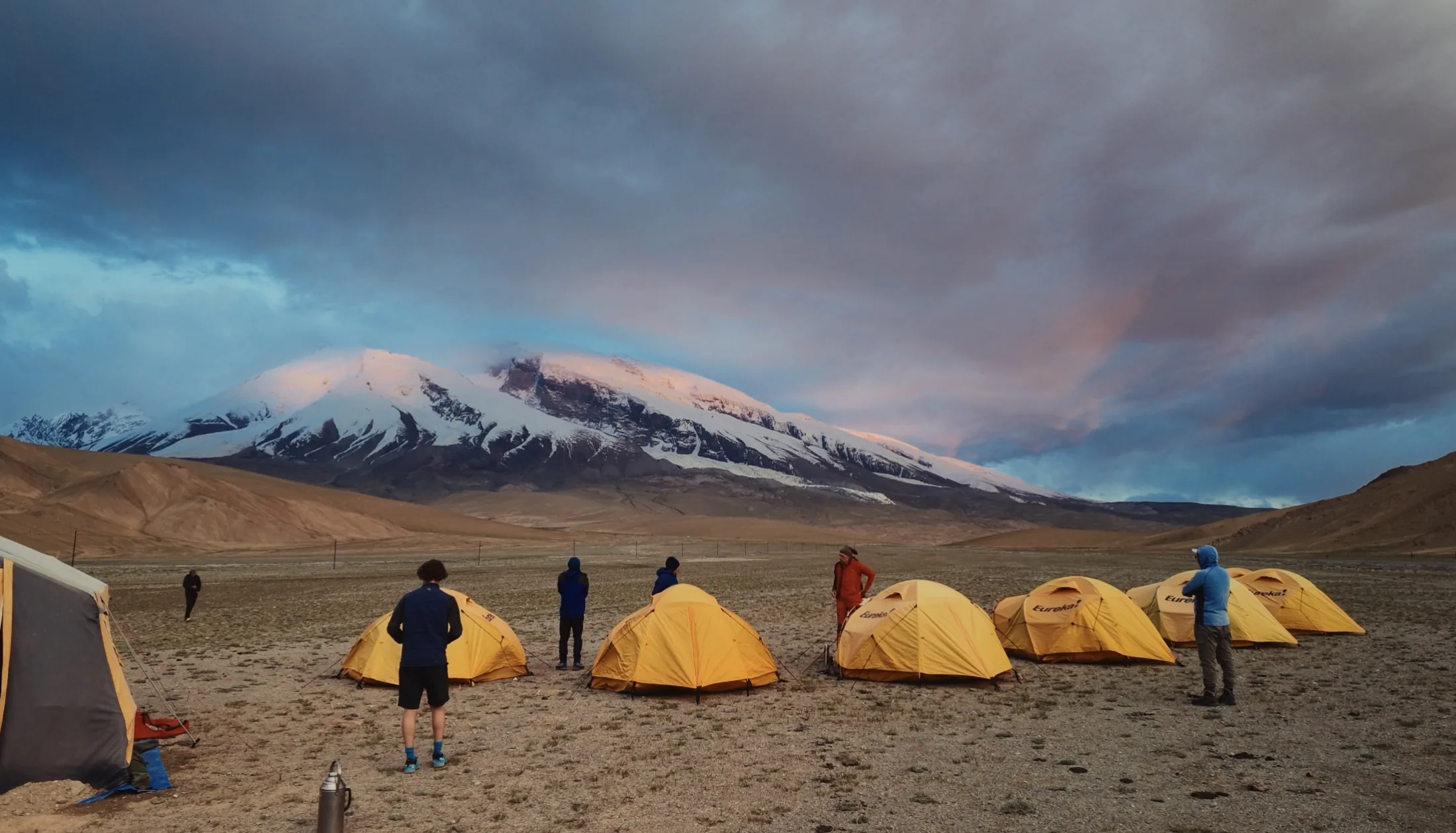 Yellow expedition tents and climbers at Subashi, also known as 204, below Muztagh Ata under dramatic evening clouds.
