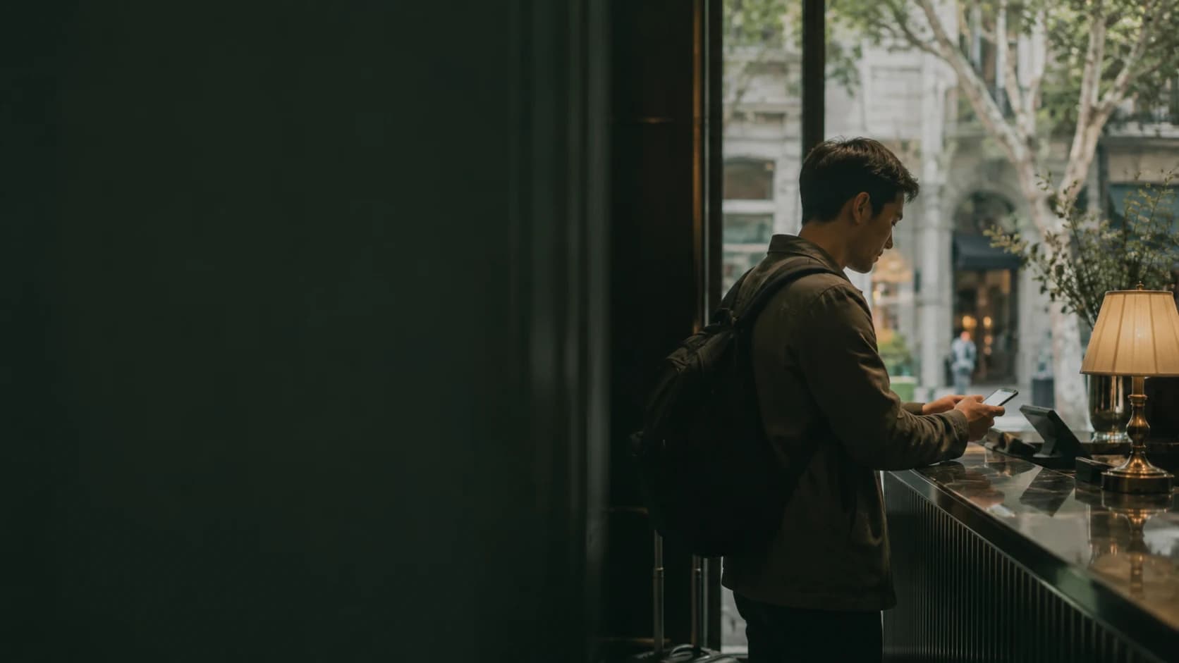 A traveller using a phone at a softly lit hotel counter.