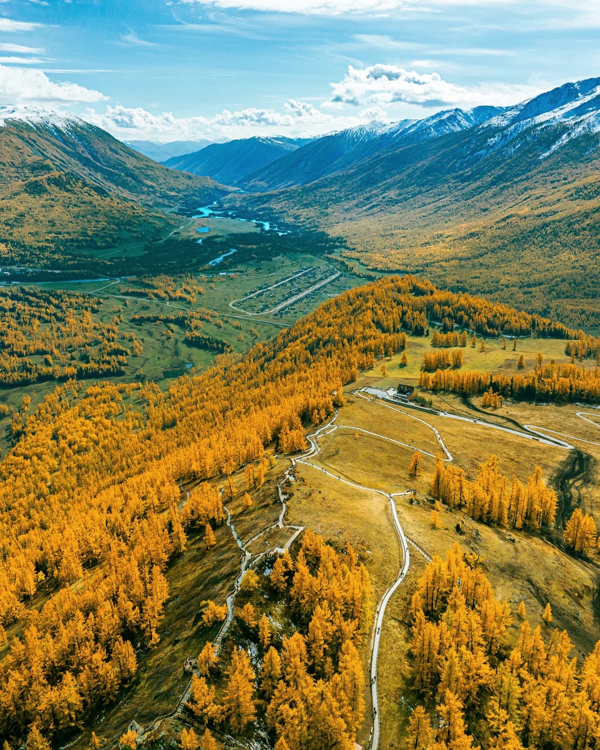 A narrow ridge and winding paths leading through golden trees towards distant mountains.