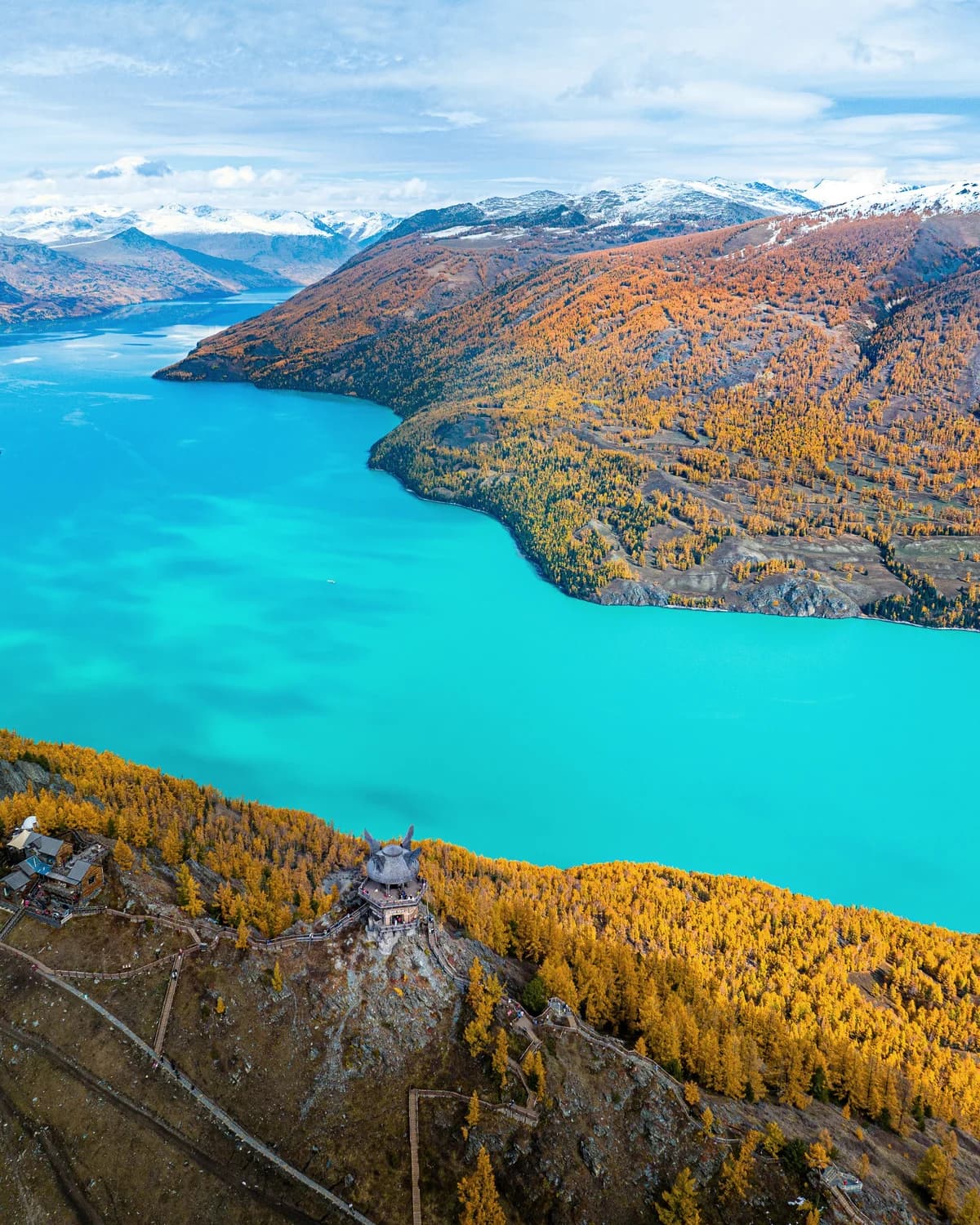 Blue-green lake water narrowing between wooded hills with autumn foliage.