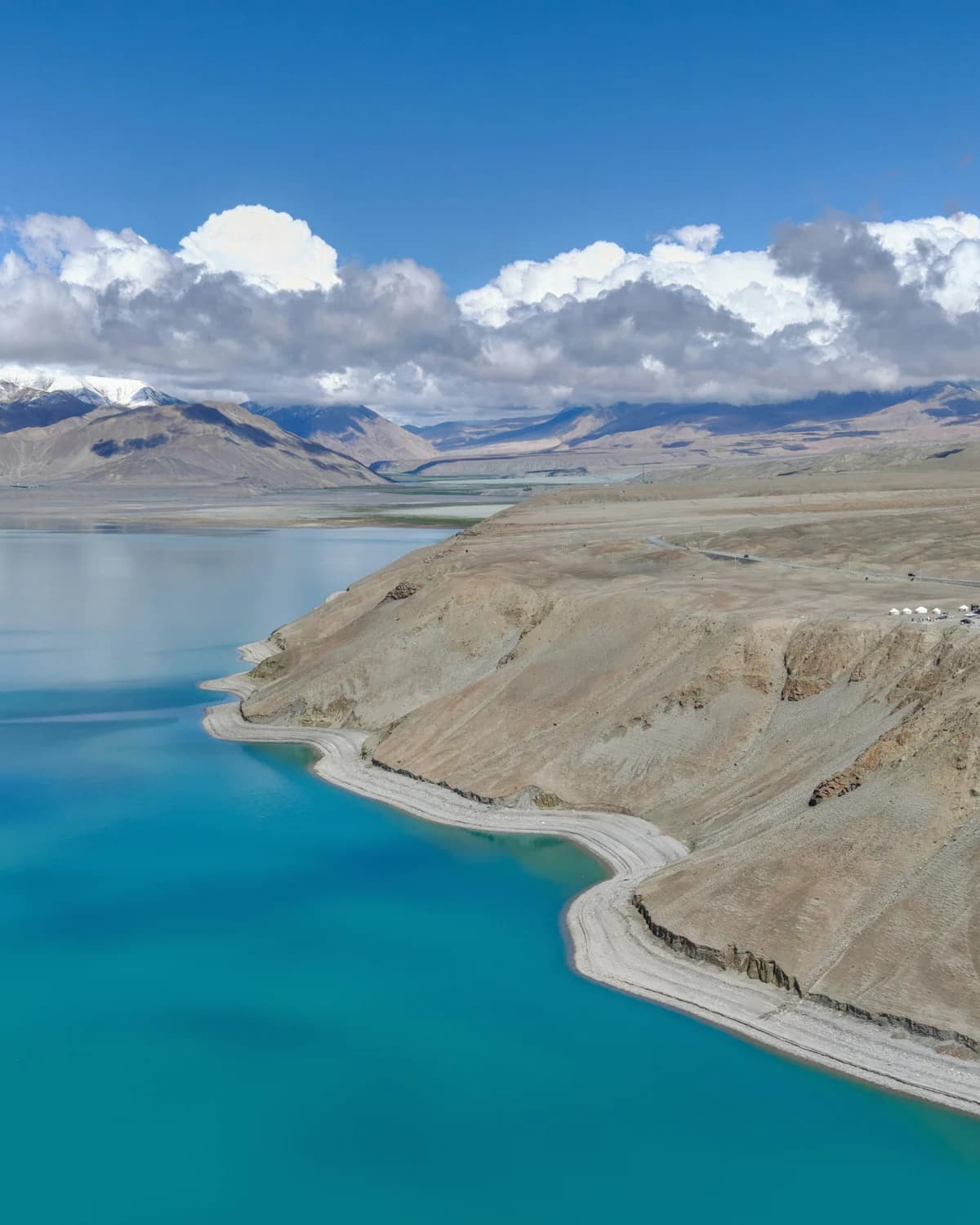A pale shoreline curving through turquoise water towards distant mountain slopes.