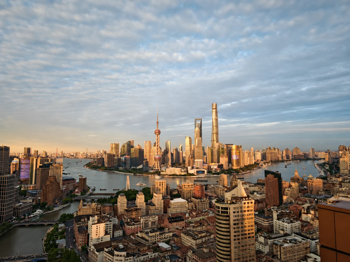 Shanghai skyline across the Huangpu River under a cloudy sky.