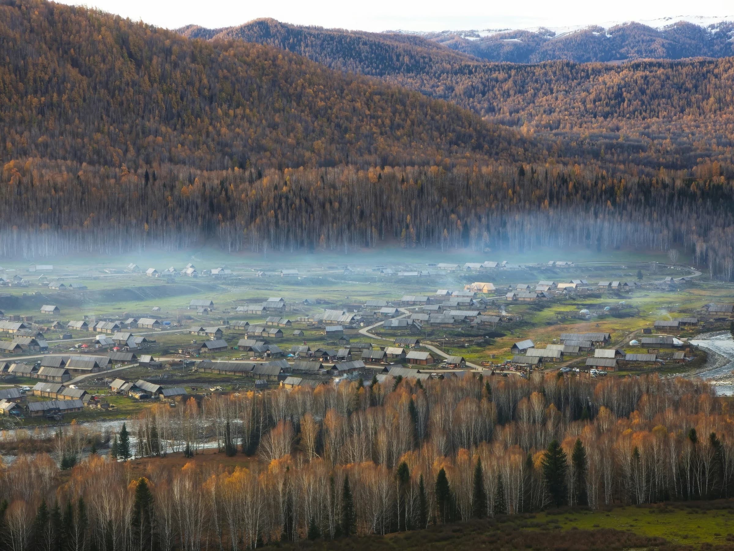Wooden houses and fields in Hemu Village beneath mist and autumn-coloured hills.