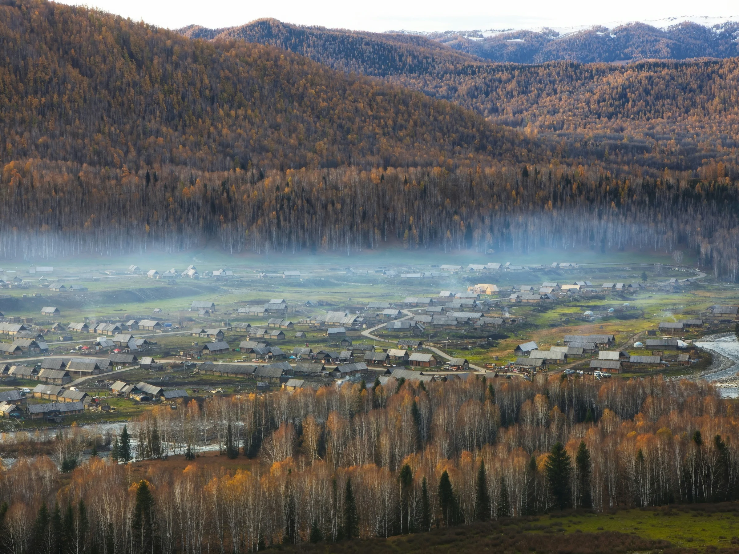 Wooden houses and fields in Hemu Village beneath mist and autumn-coloured hills.